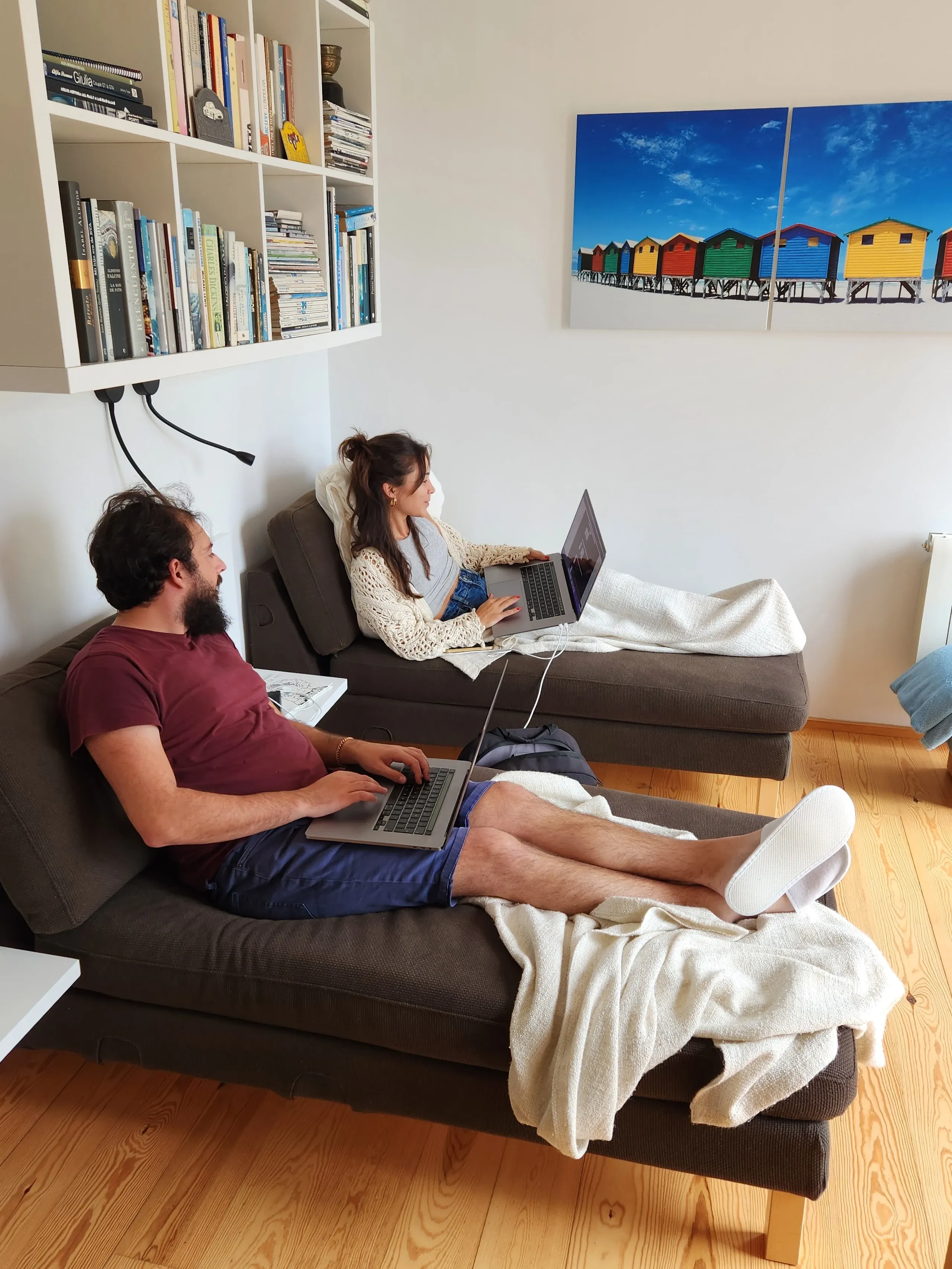 Two concealed members sitting and working together. One is showing their computer screen to the other.